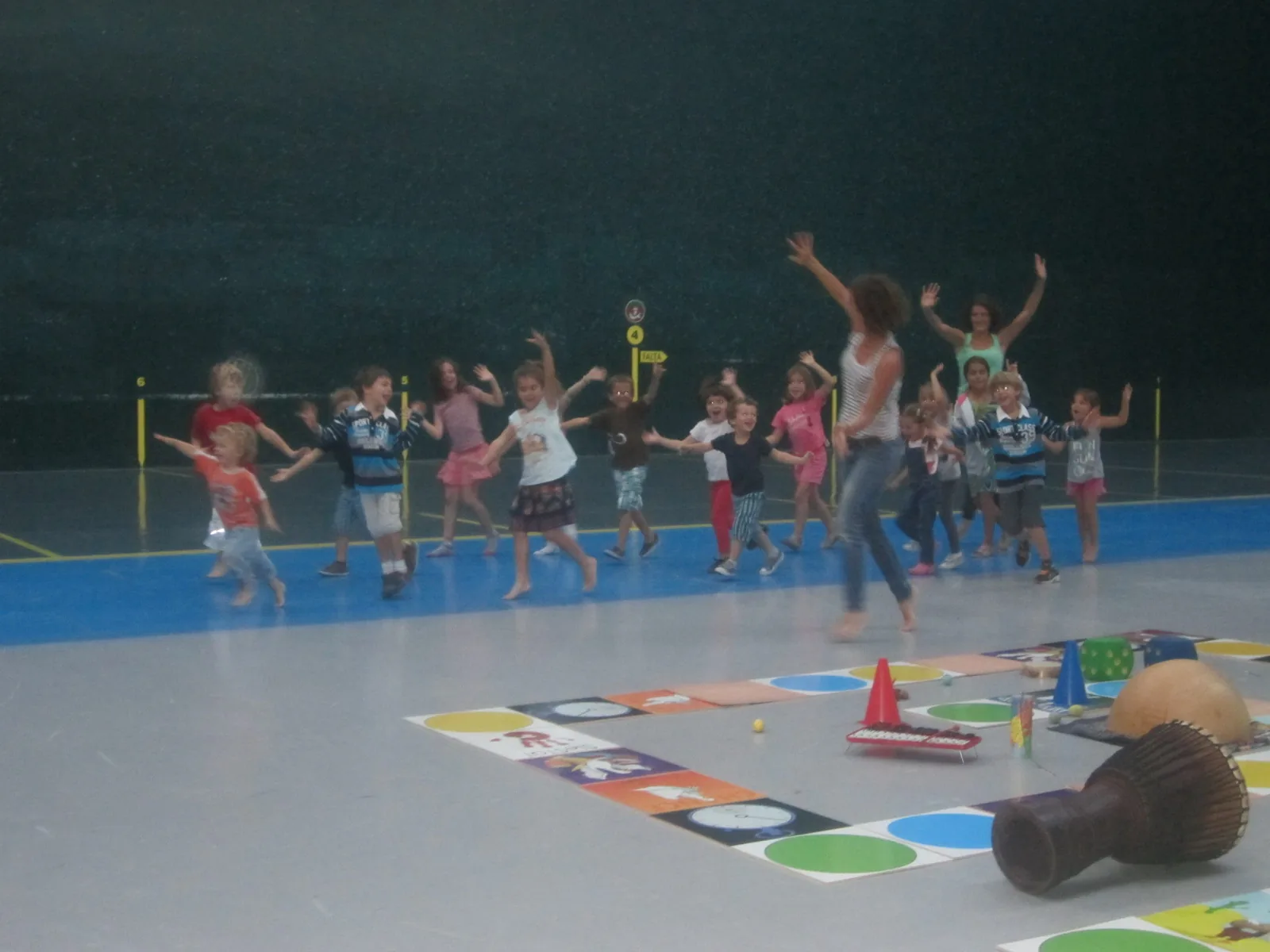 Dans un gymnase, des enfants dansent et sautent autour du plateau de jeu.