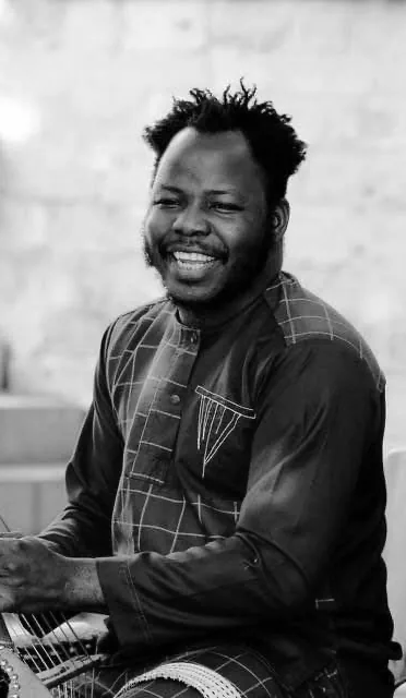 Portrait en noir et blanc de Mamadou Dembélé, souriant, assis à la kora.